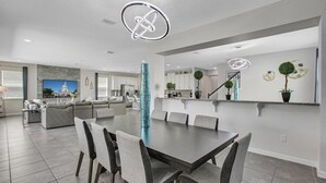 A modern kitchen with white cabinets, a central island, and a dining area with a dark table and grey chairs. - Cvt1749 (Kissimmee)