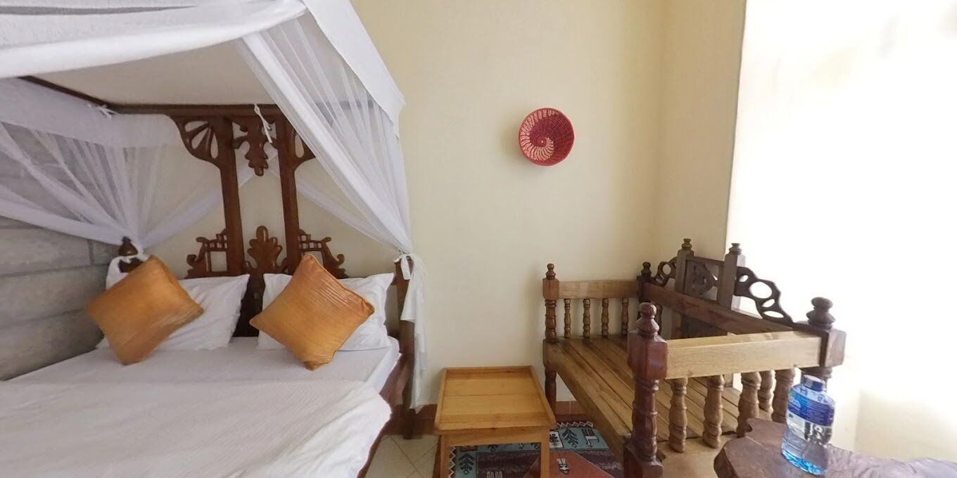A room with a bed under a canopy, a wooden bench, a small table, and a wall-mounted decorative plate.