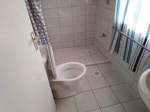 Pieni, laatoitettu kylpyhuone, jossa on wc, suihkutila ja pesuallas.