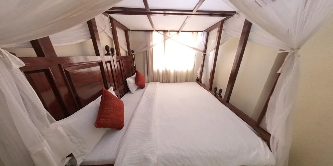 A room with a bed, white curtains, and a wooden headboard.