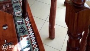 Uma mesa de jantar de madeira com cadeiras, um tapete estampado e um enfeite de parede.