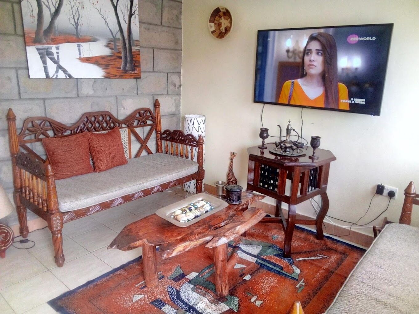 A living room with a wooden sofa, a coffee table, and a television mounted on the wall.