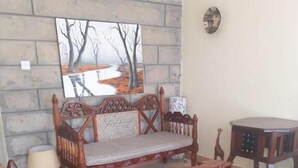 Uma sala de estar com parede de pedra, um banco de madeira, uma mesa pequena e um tapete.