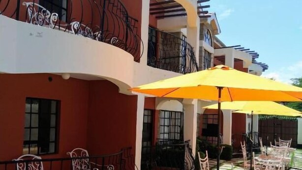 Um pátio com área de estar externa, um guarda-sol amarelo e um edifício com sacadas.