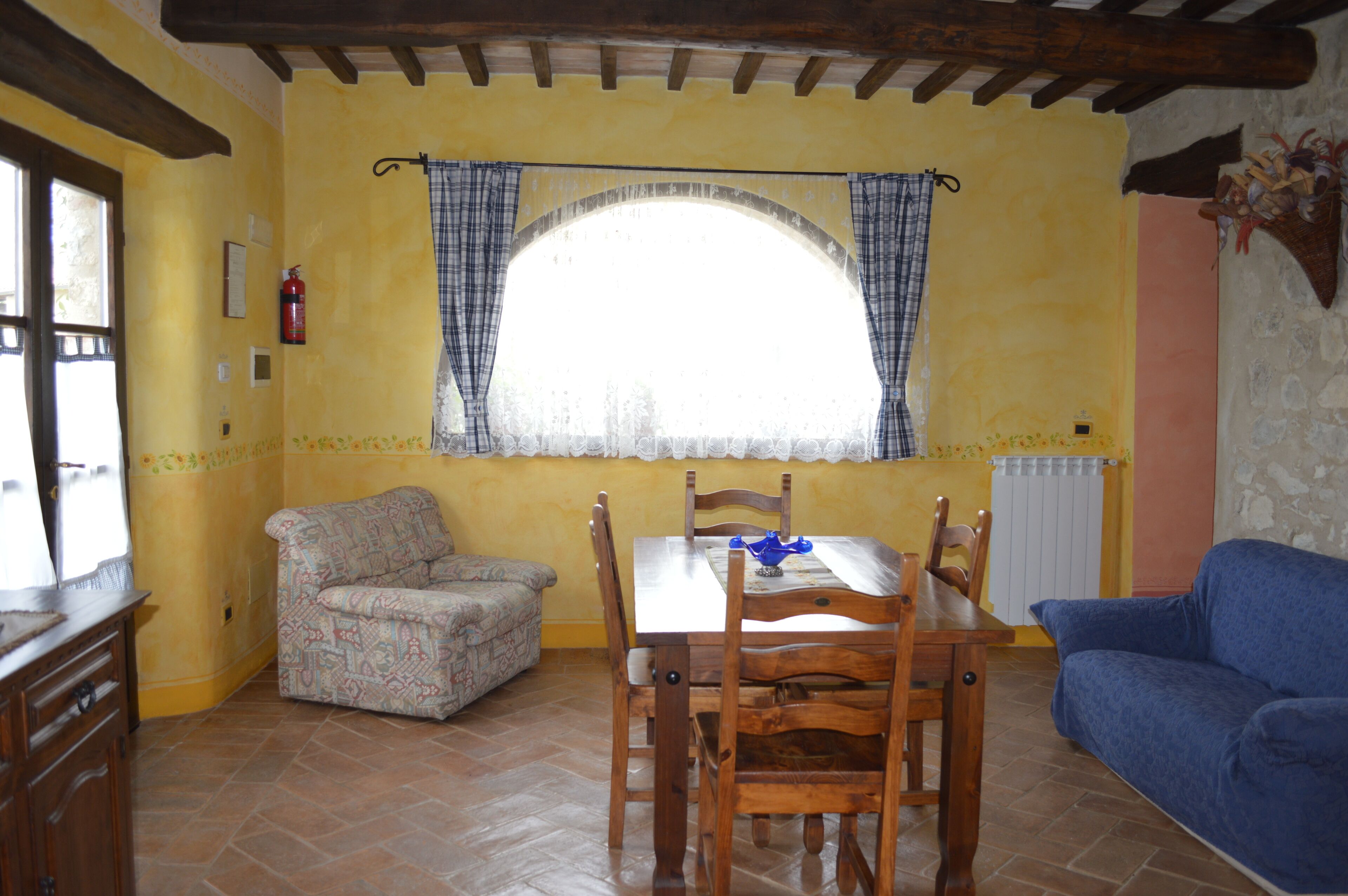 Un comedor con una mesa y sillas, un sofá estampado y una ventana con cortinas.