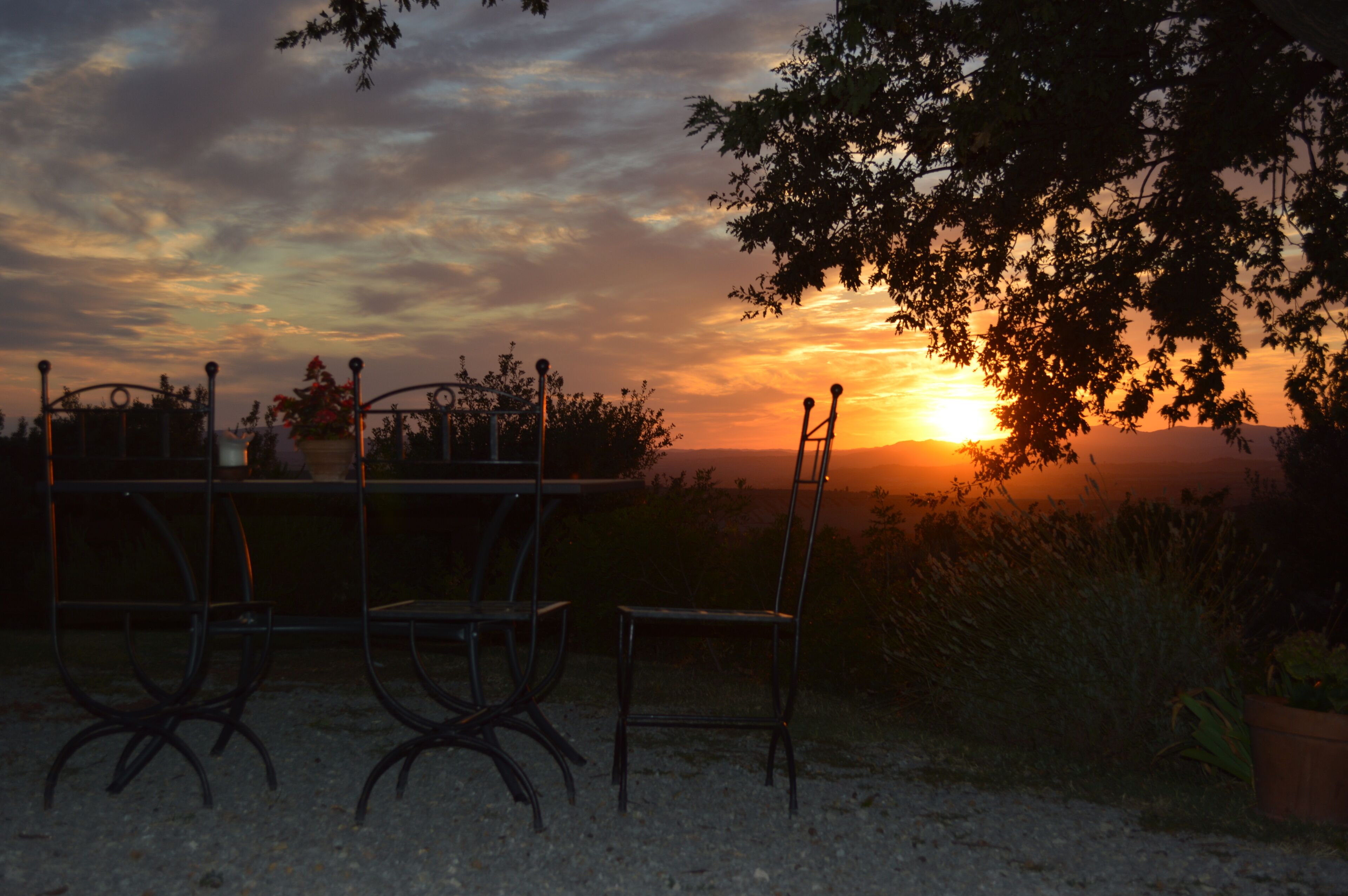 A sunset view with a metal table and chairs, surrounded by trees and a clear sky.