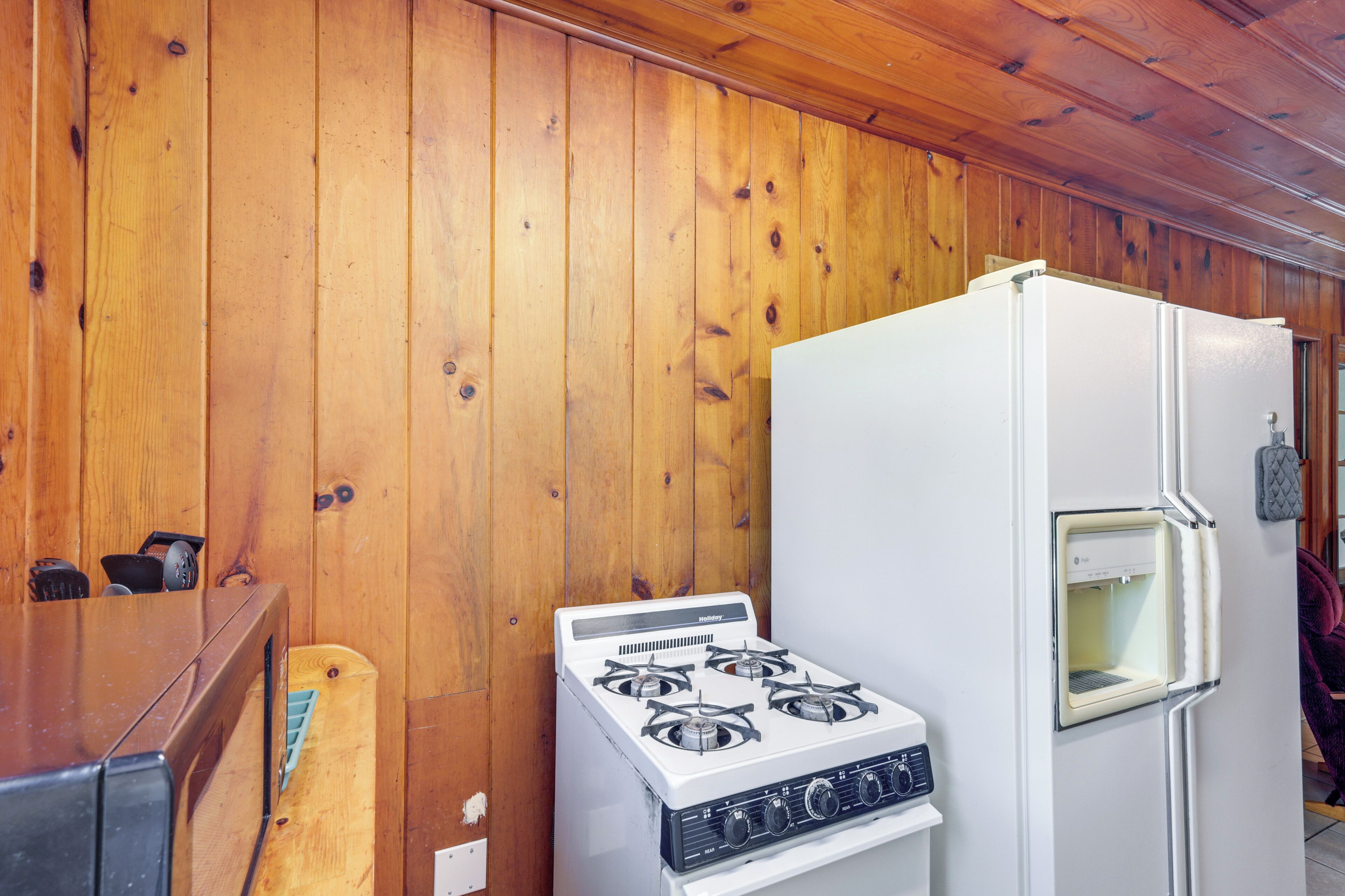 Une cuisine avec des murs en bois, un poêle blanc et un réfrigérateur.
