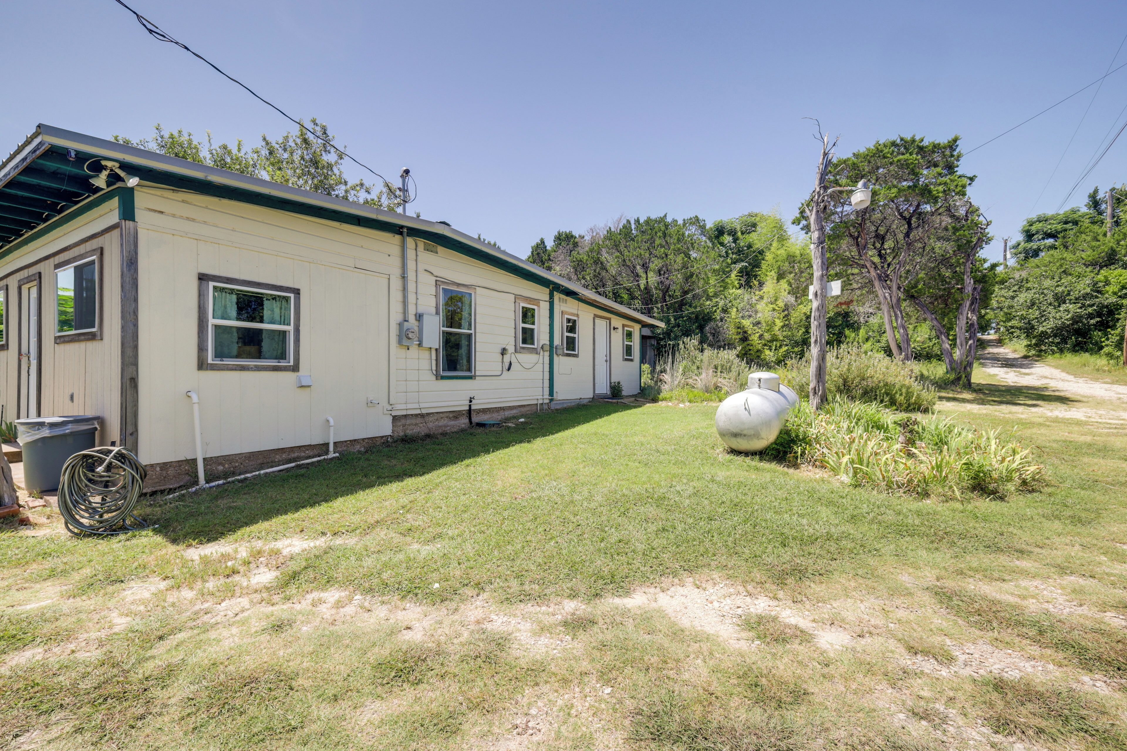 A single-story mobile home with a covered porch, a small front yard, and a large white water tank.