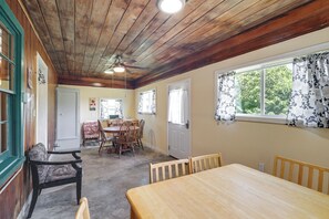 Un espace repas avec des tables et des chaises en bois, un ventilateur de plafond et des fenêtres ornées de rideaux à motifs.