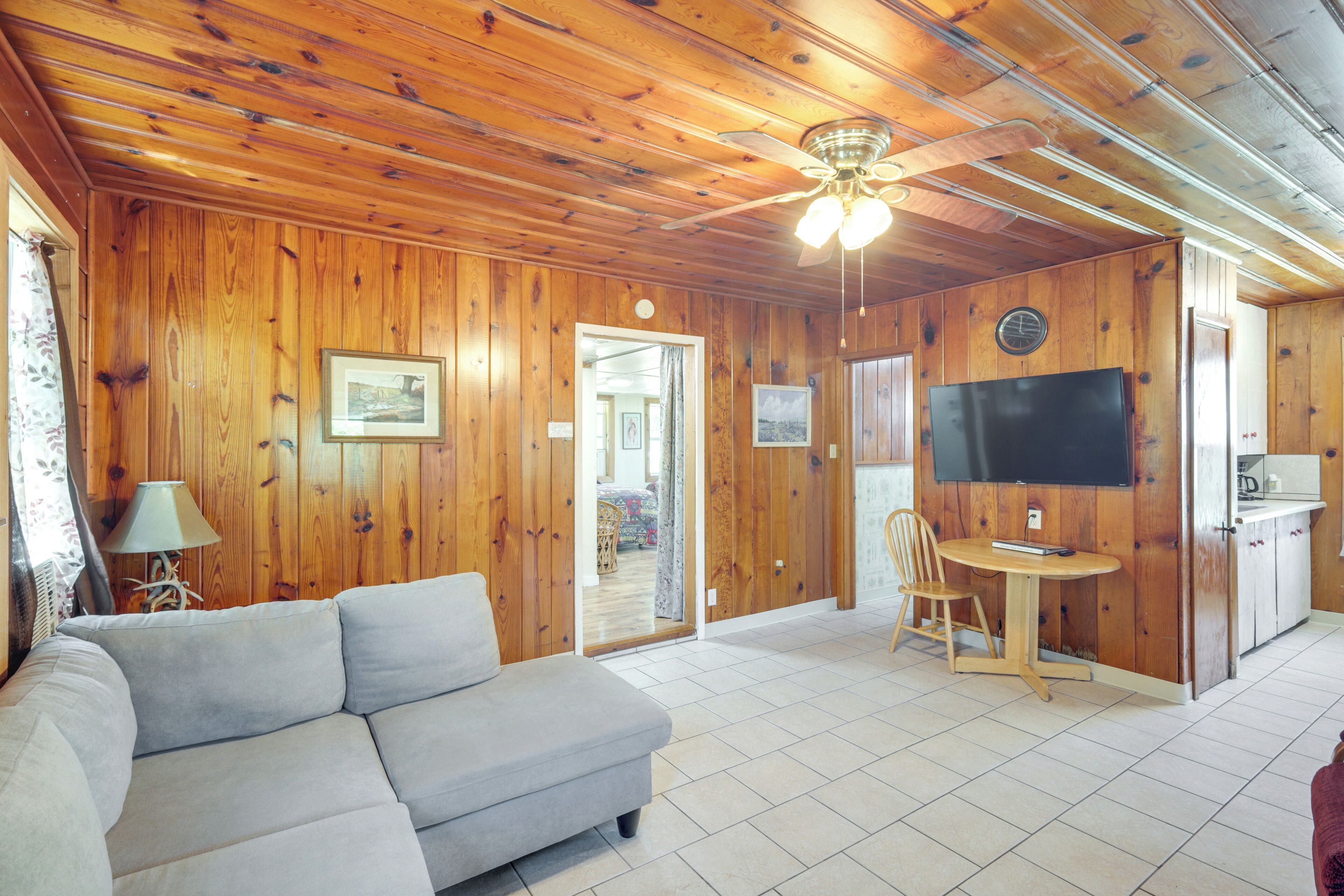 A wooden-paneled room with a sofa, a dining table with chairs, a ceiling fan, and a flat-screen TV.