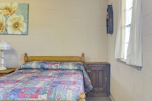 Un dormitorio con una cama de madera, un colcha, una mesita de noche, una lámpara, un armario y una ventana con cortinas.