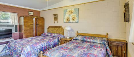 A bedroom with two beds, a ceiling fan, a television, and a window with curtains.
