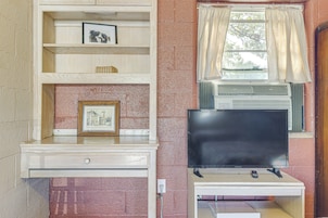 Una habitación con televisión sobre un mueble, una ventana con cortinas y un estante con marcos de fotos.