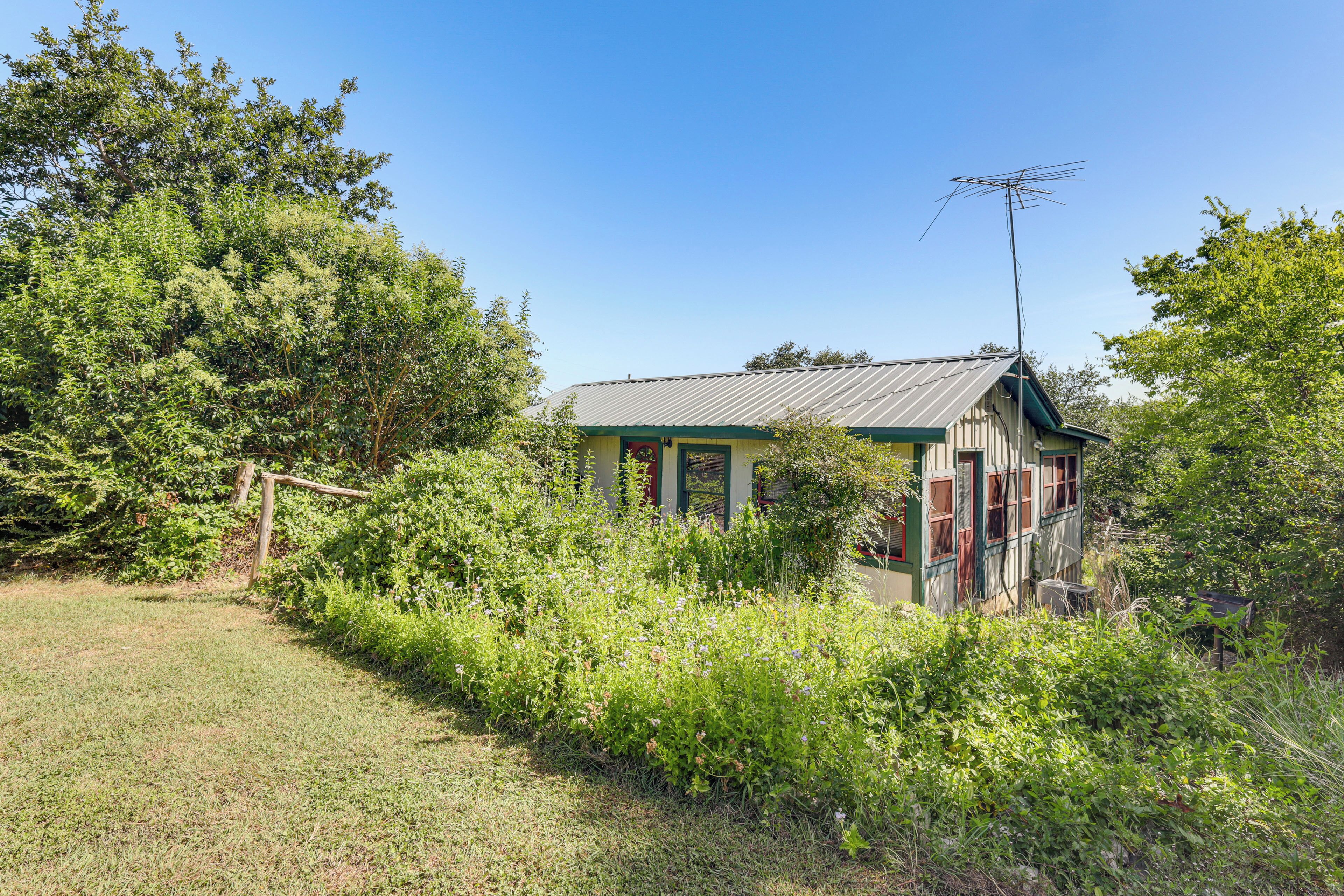 A small, rustic house with a metal roof, surrounded by dense greenery and trees.