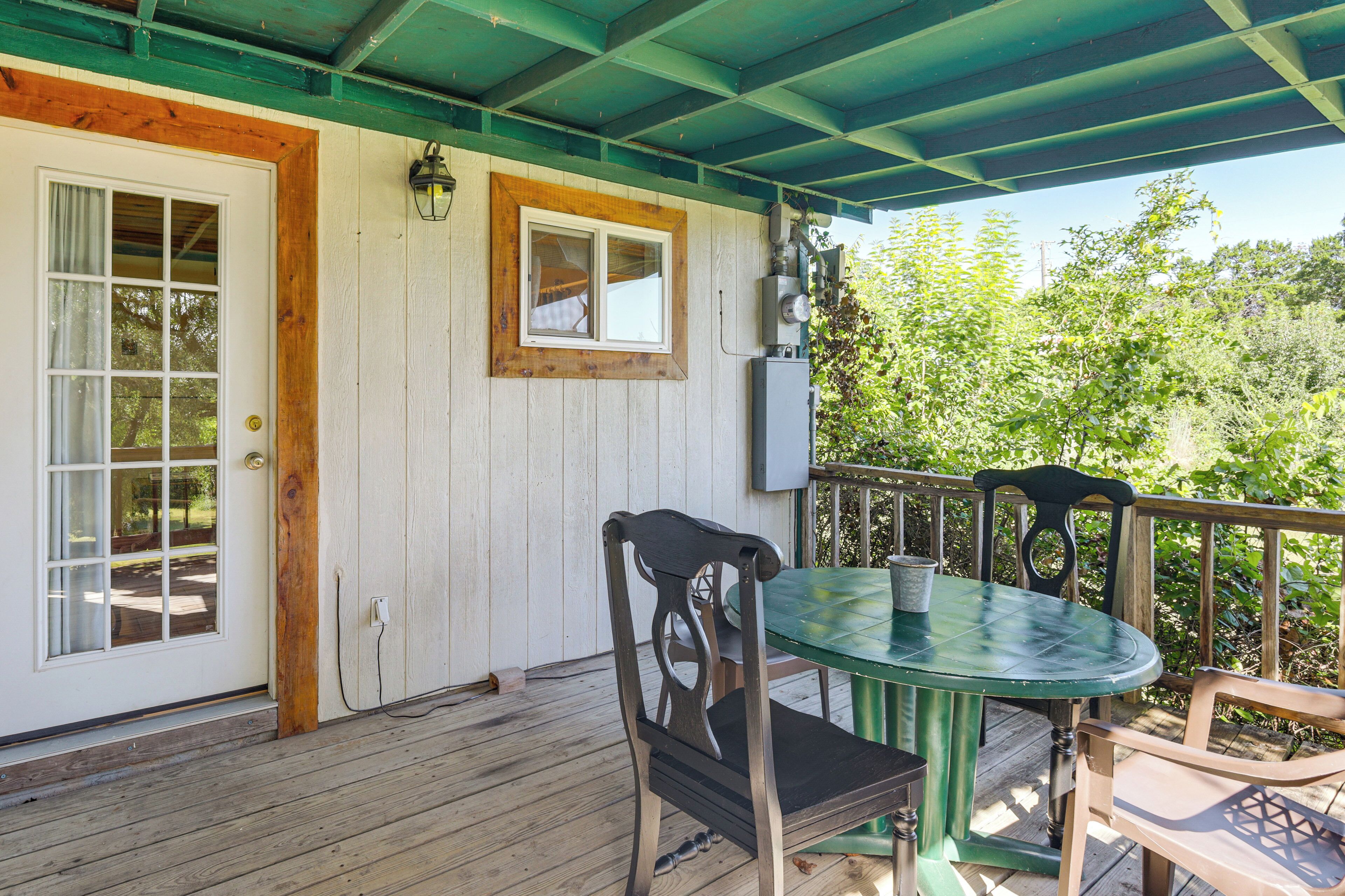 A wooden deck with a green table and chairs, a door, and a window.