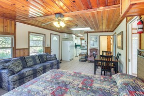 A cozy room with a large bed, a sofa, a dining table with chairs, a ceiling fan, and a kitchen area in the background. - Trails On-site! Pet-friendly Lake Whitney Cottage (Whitney)