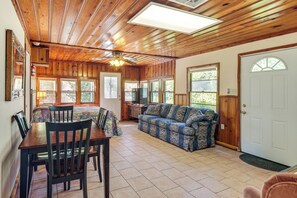 A spacious living area with a wooden ceiling, a sofa, a dining table with chairs, and large windows. - Trails On-site! Pet-friendly Lake Whitney Cottage (Whitney)