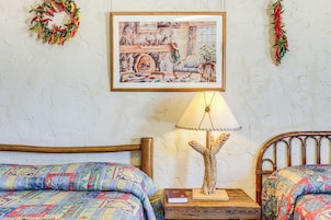 Una habitación con dos camas, un cuadro en la pared, una lámpara sobre una mesita de noche de madera y un adorno de guirnalda.
