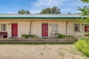 Un edificio con techo verde, dos puertas rojas y un pequeño espacio exterior con mesa y sillas.