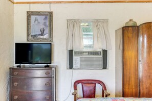 Una habitación con un aparador de madera, televisión, aire acondicionado, una silla y un armario.