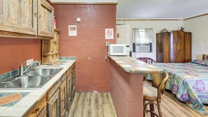 A compact kitchen with a sink, wooden cabinets, and a microwave. There is a small dining area with a chair and a bed with a colorful quilt. - Studio w/ Trail Access: 8 Mi to Lake Whitney St Pk (Whitney)