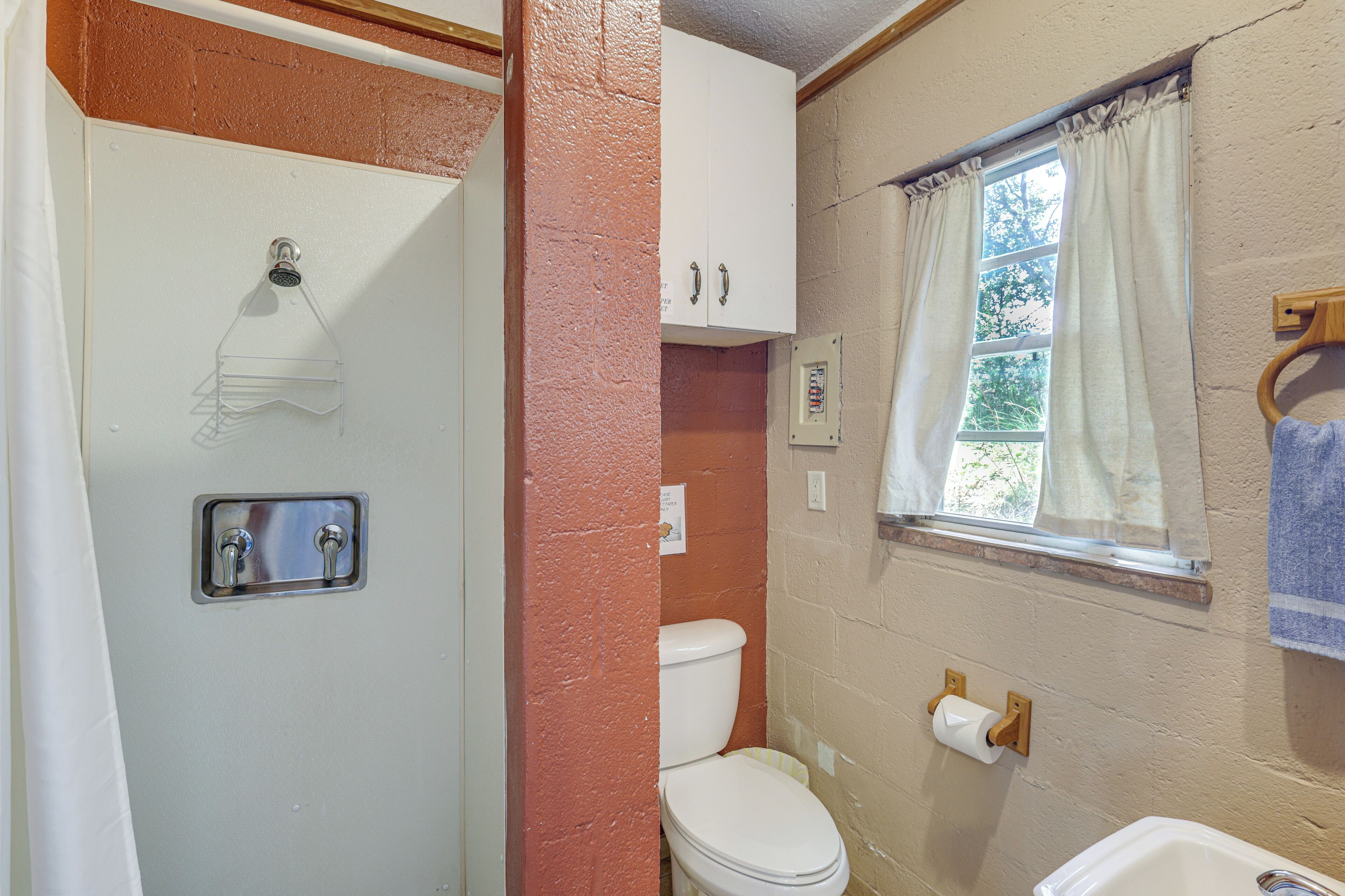 Et badeværelse med bruser, toilet og vindue.