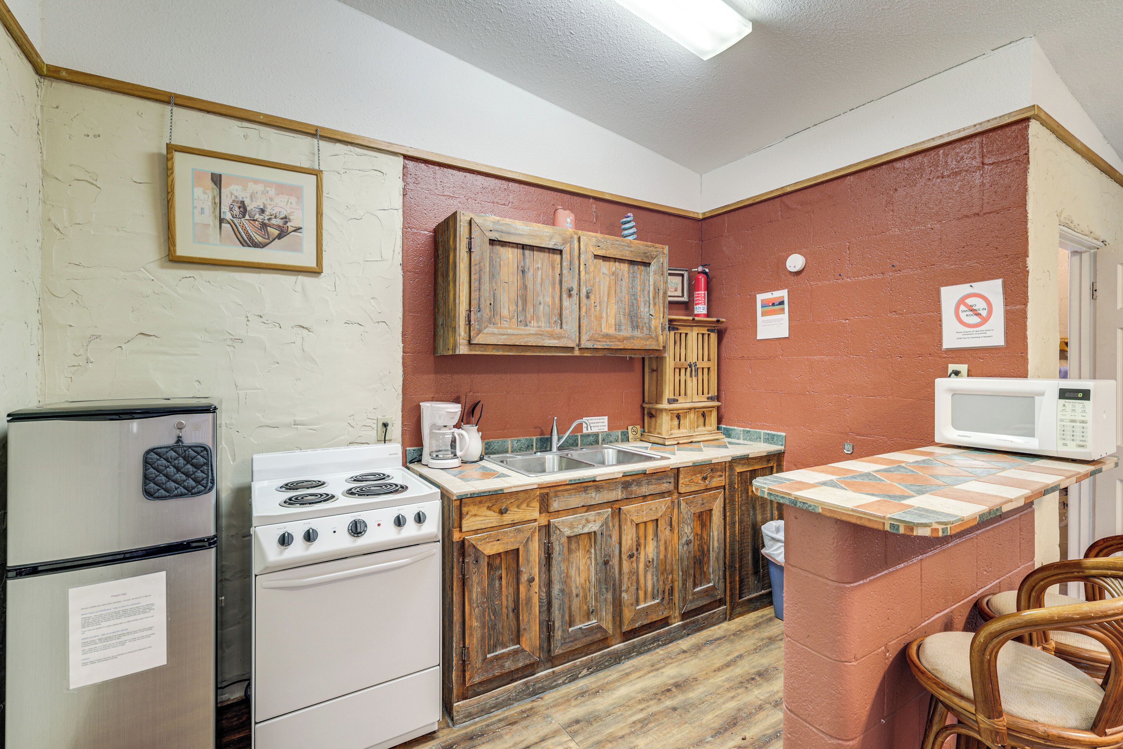 A compact kitchen with a refrigerator, stove, wooden cabinets, a microwave, and a small island with chairs.