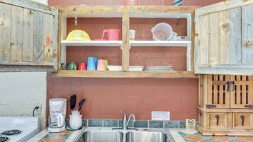 A kitchen with a sink, a coffee maker, and a cabinet with dishes and utensils.