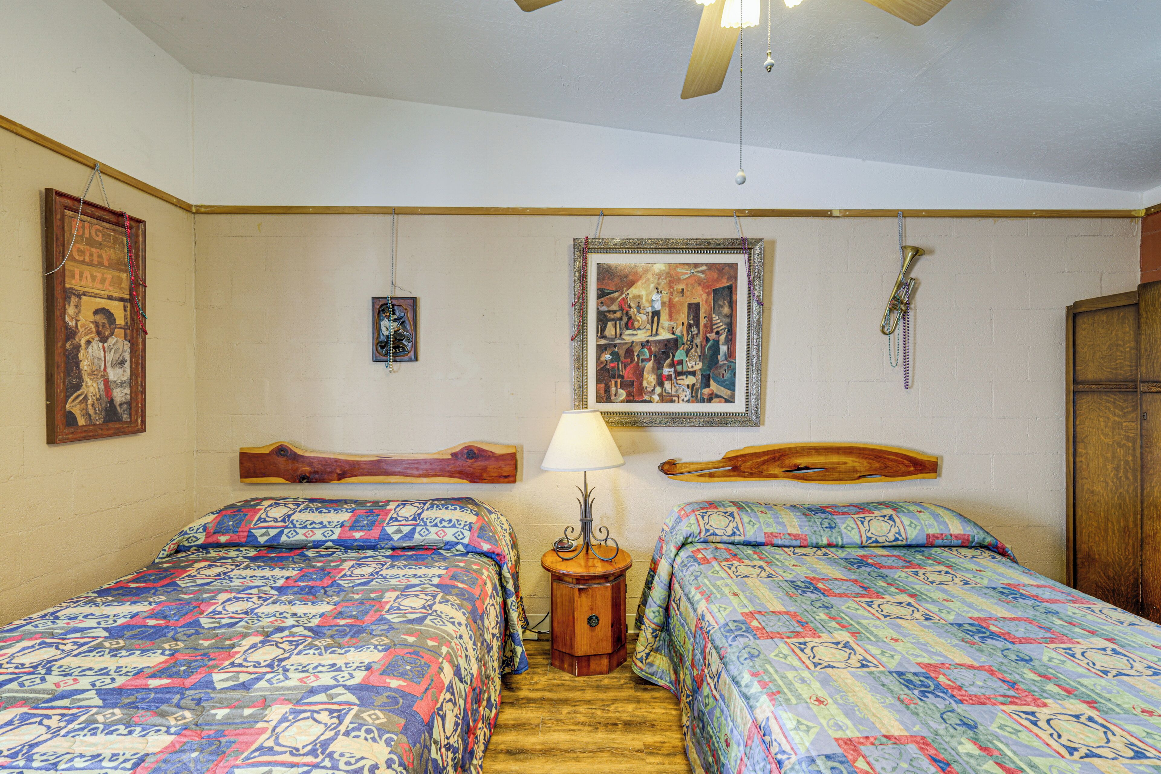 Een kamer met twee bedden, een houten hoofdbord, een nachtkastje van hout met een lamp, en een messing trompet aan de muur.