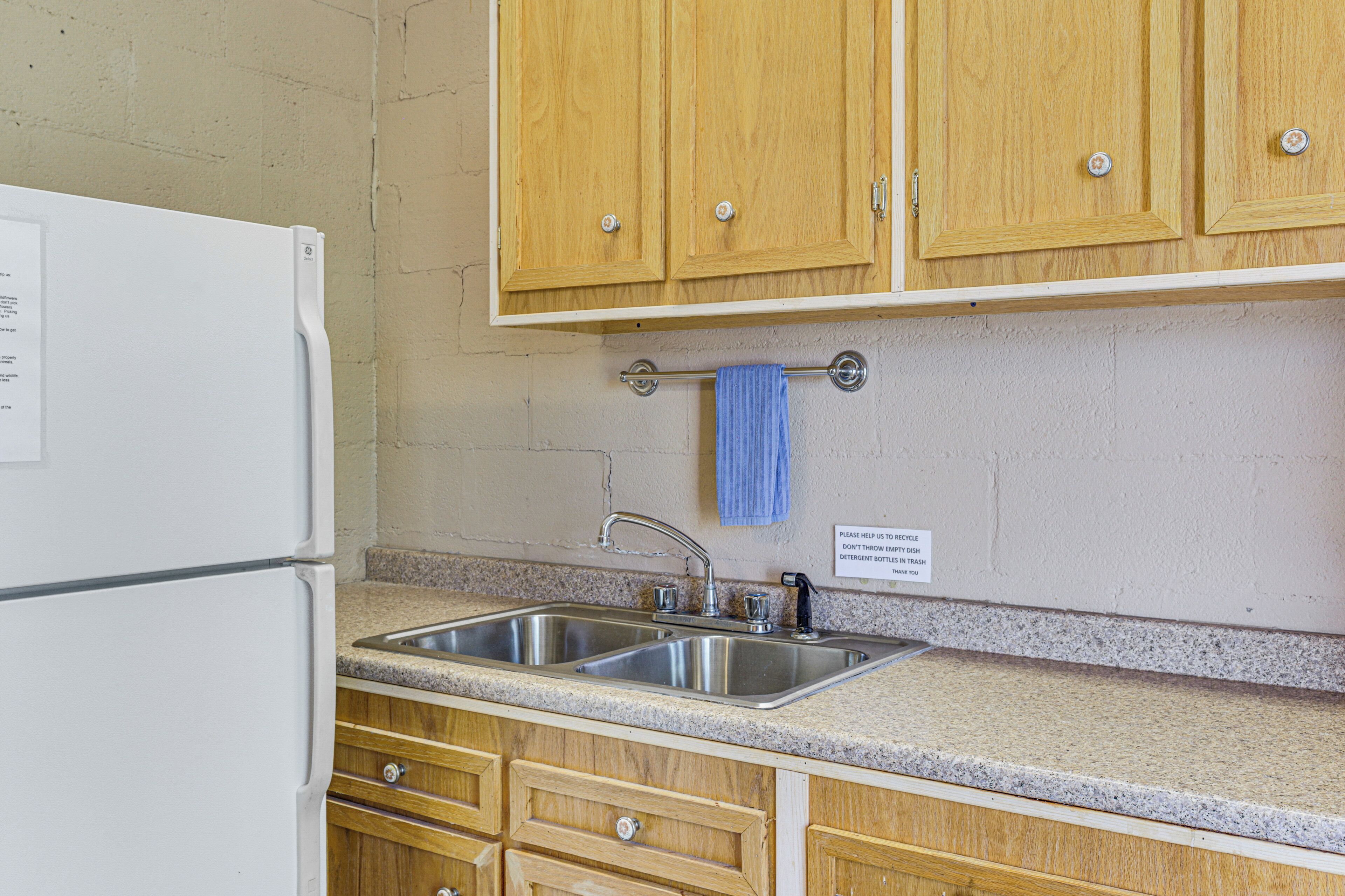 Una cocina con armarios de madera, un lavamanos de acero inoxidable y un refrigerador blanco.