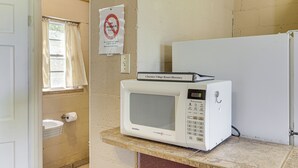 Microondas blanco sobre una encimera de mármol en una habitación con paredes color beige, una puerta blanca y una ventana con cortinas.
