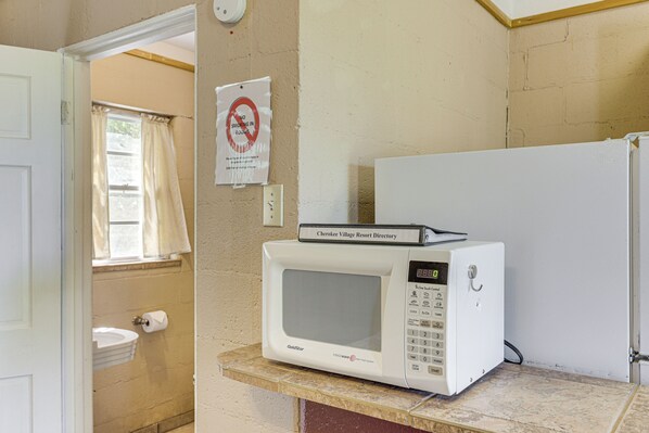A white microwave on a countertop in a room with beige walls, a door, and a window with curtains.