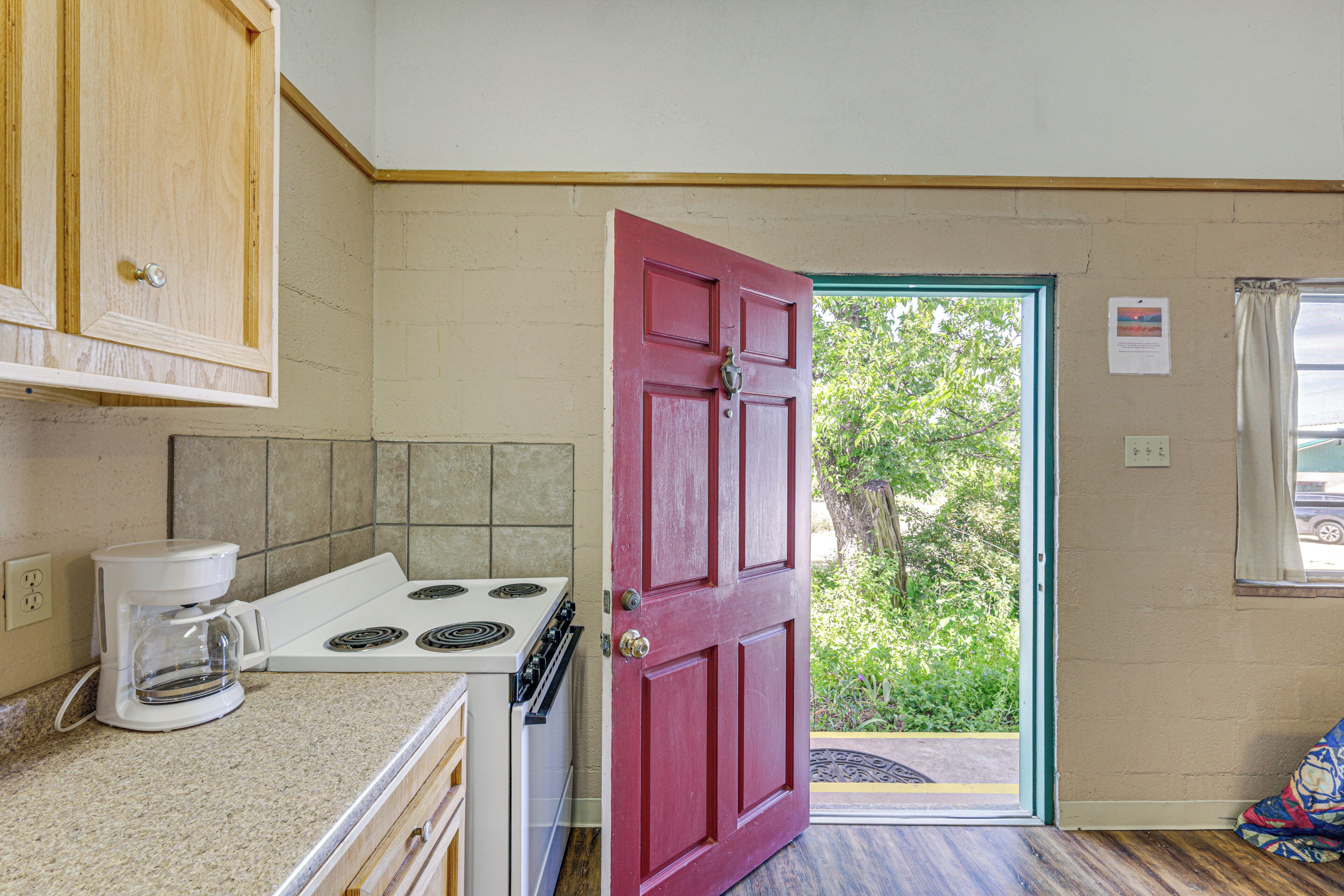 Una cocina con una puerta roja, una estufa y una cafetera.