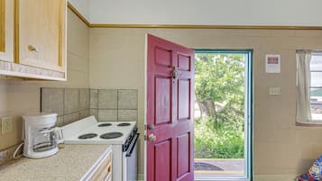 Una cocina con una puerta roja, una estufa y una cafetera.