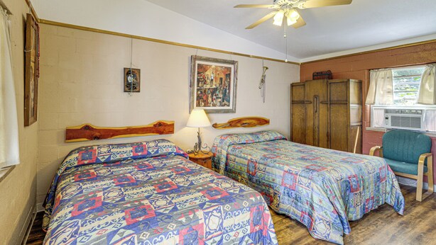 Un dormitorio con dos camas, un ventilador de techo, una ventana con cortinas y un armario de madera.