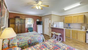 Habitació d'hotel senzilla amb dos llits, una cuineta, un ventilador de sostre i una finestra amb cortines.
