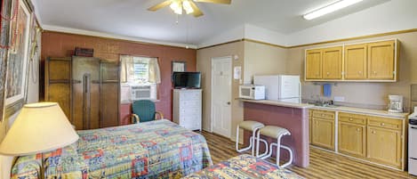 Habitación de hotel pequeña con dos camas, una kitchenette, un ventilador de techo y una ventana con cortinas.