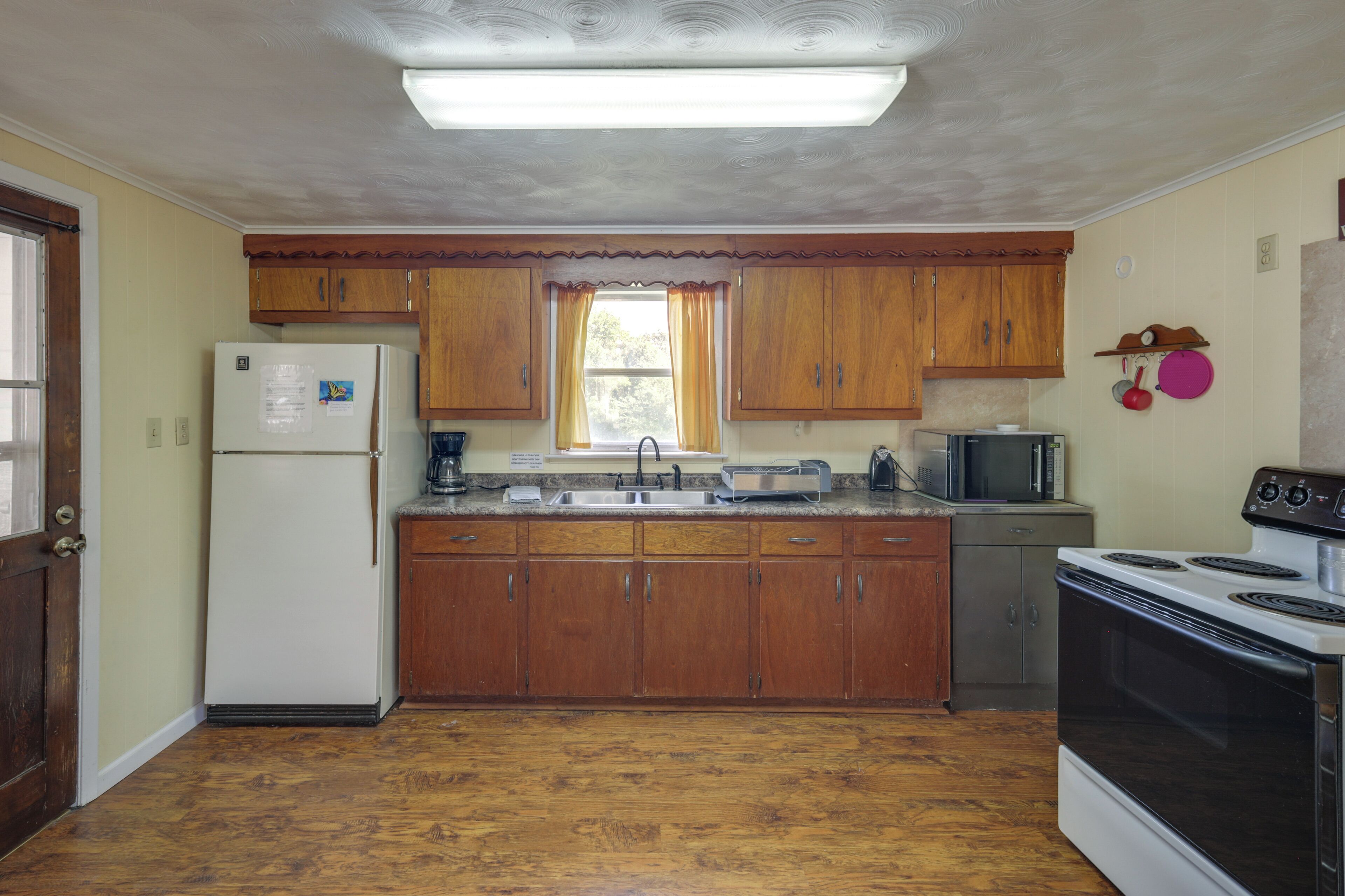 Une cuisine avec des meubles de rangement en bois, un réfrigérateur, un four à micro-ondes, une cuisinière et une fenêtre avec des rideaux.