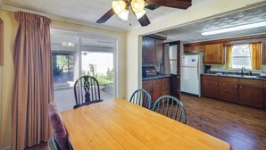 Un coin repas avec une table et des chaises en bois, un ventilateur de plafond et une vue sur le jardin à travers une porte-fenêtre coulissante.