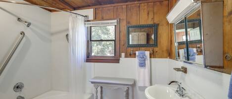 Une salle de bain avec une baignoire, un lavabo, un meuble-lavabo et une fenêtre.