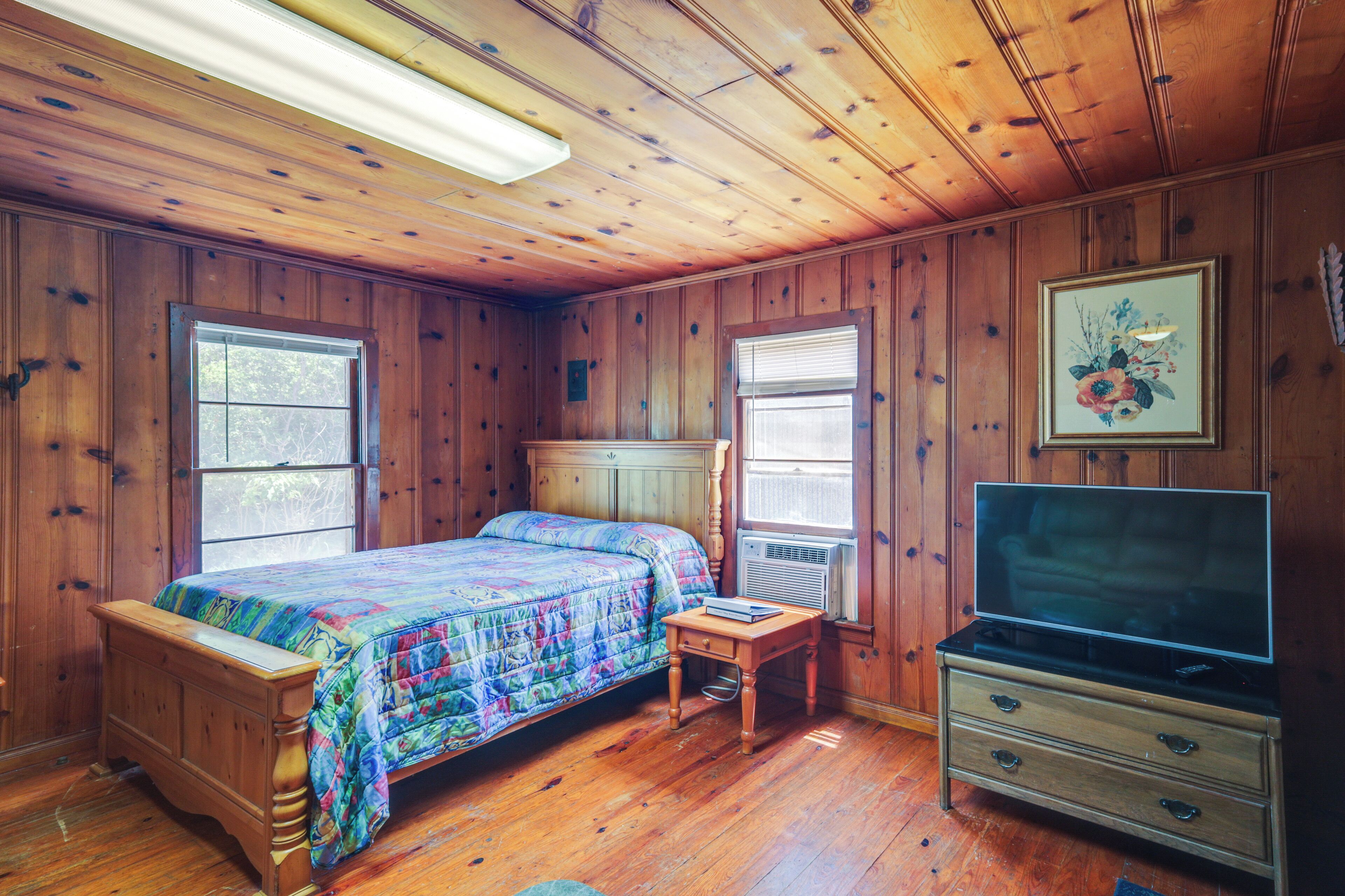 A wooden-paneled bedroom with a bed, a dresser, and a television.