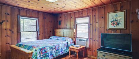 A wooden-paneled bedroom with a bed, a dresser, and a television.