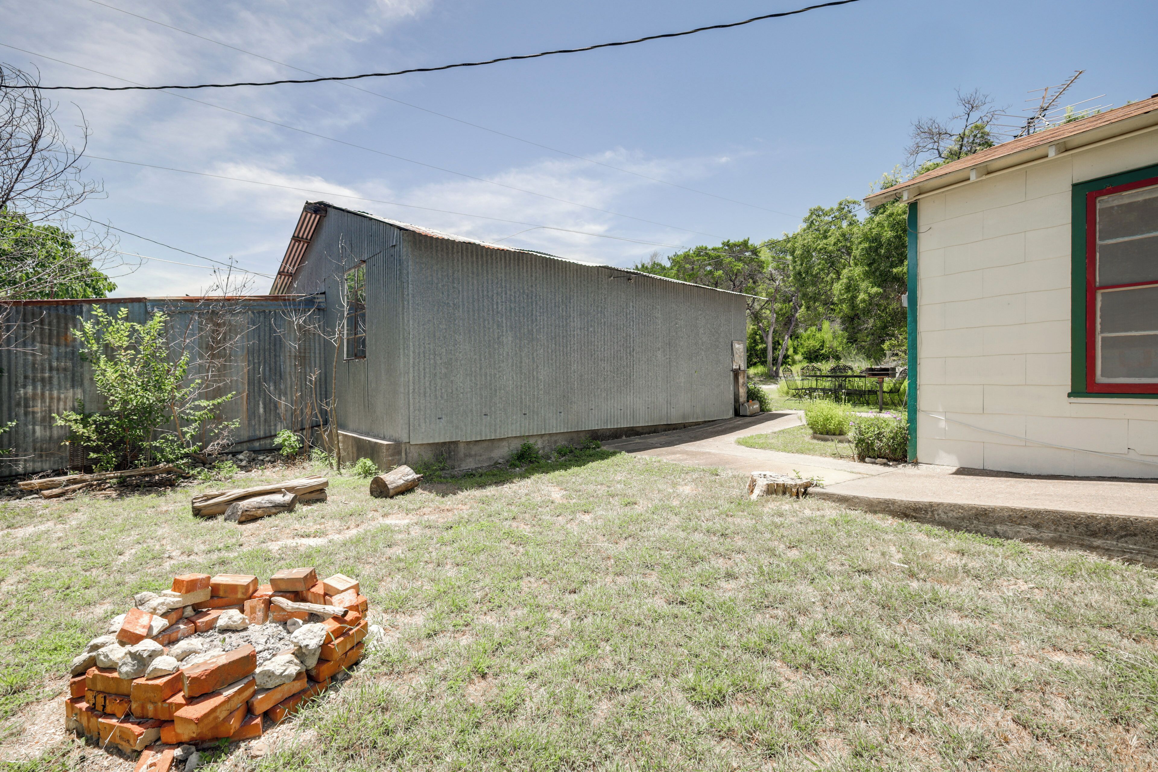 A backyard with a corrugated metal shed, a brick wall, and a small building with a red window.