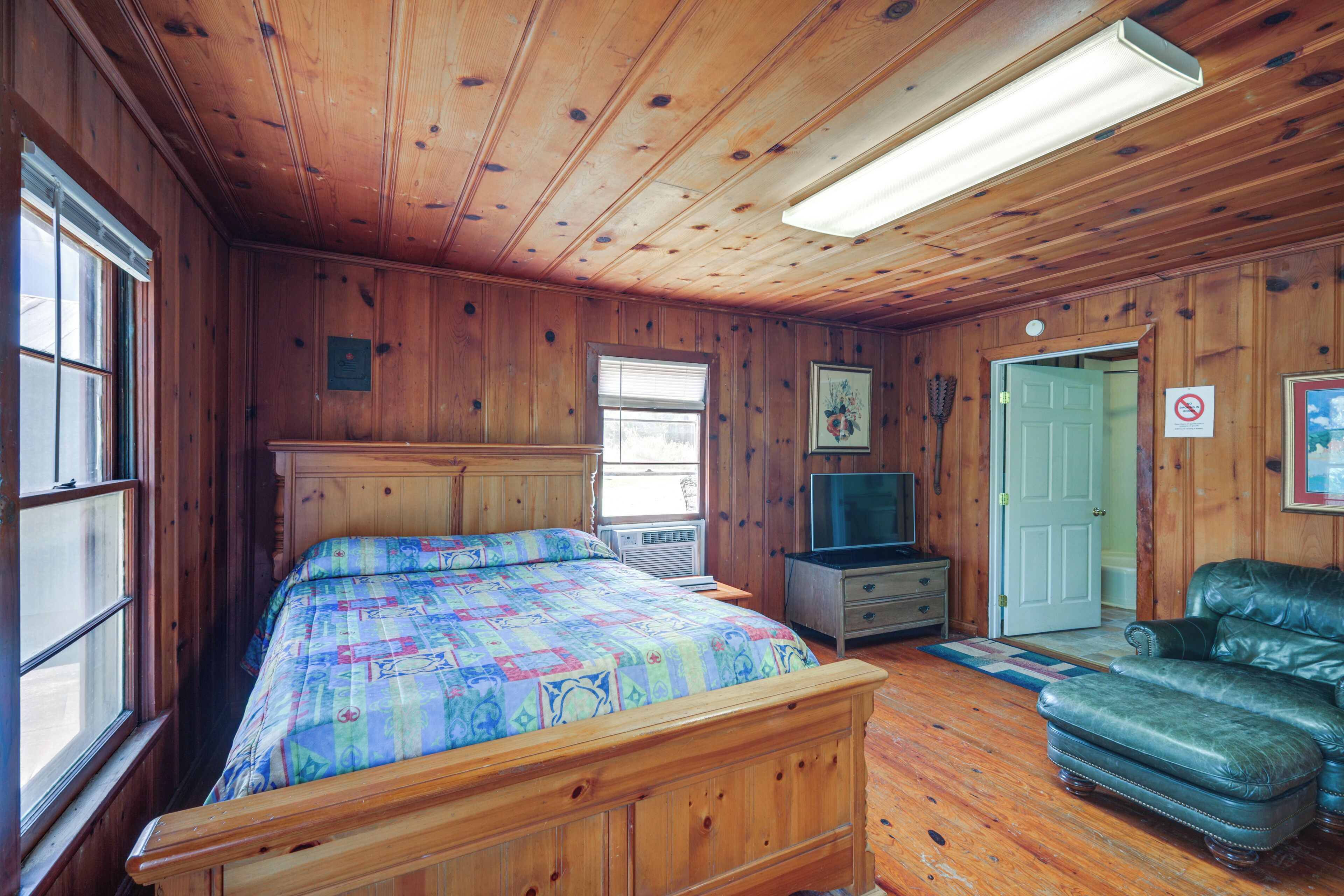 A wooden cabin bedroom with a bed, a television, a leather couch, and a door.