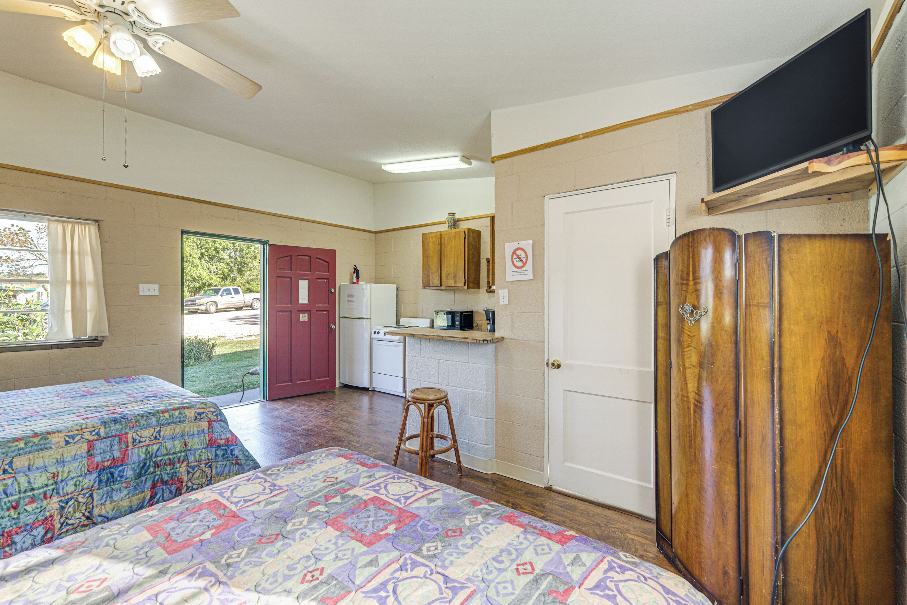 A room with two beds, a kitchenette, a bathroom, and a TV mounted on the wall.