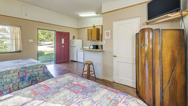 Une chambre avec deux lits, un coin cuisine, une salle de bain et un téléviseur fixé au mur.