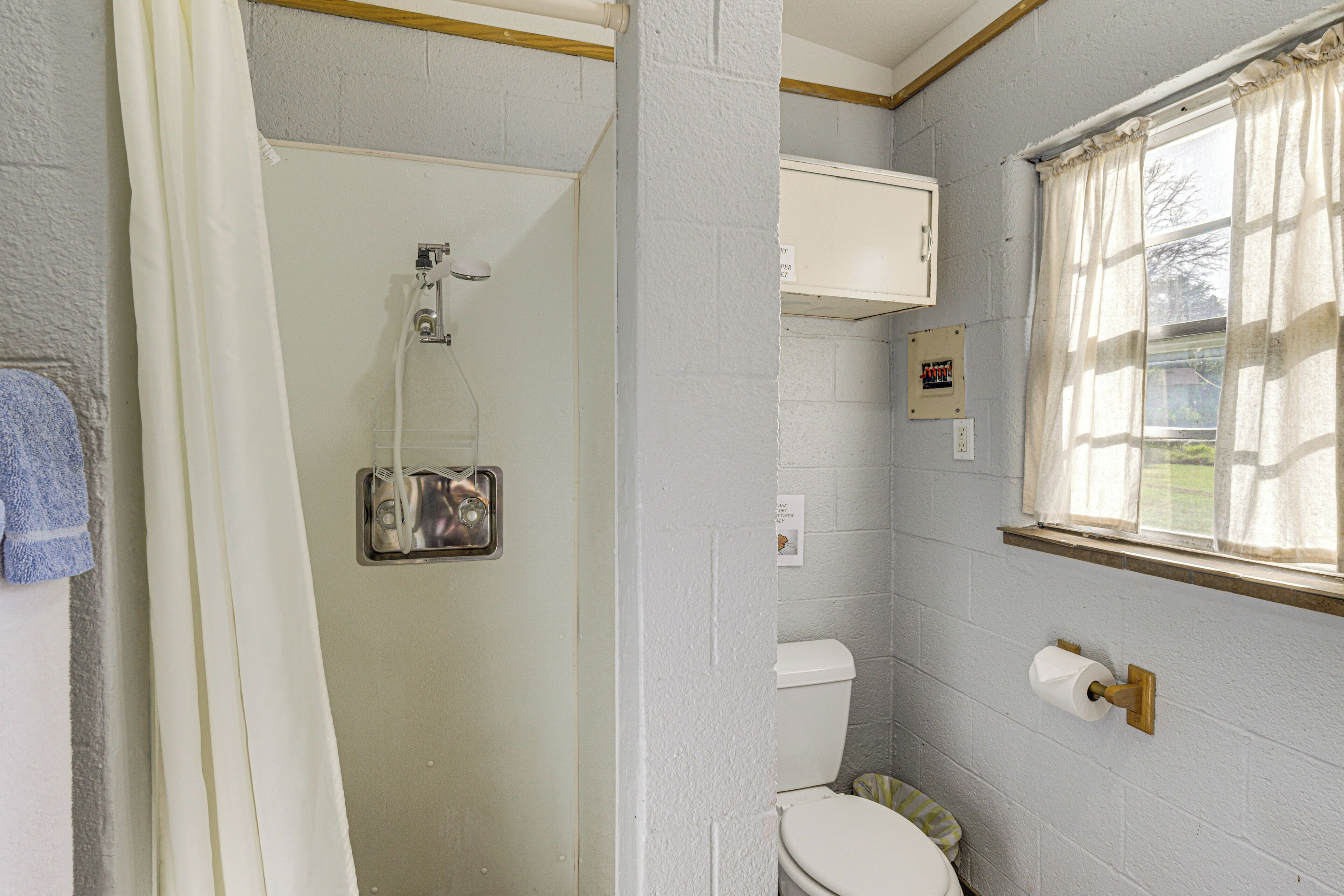 Un bagno con doccia, WC e finestra con tende.
