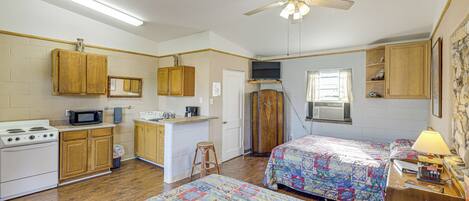 Estudio compacto con kitchenette, dos camas, ventilador de techo y una pared de acento de piedra.