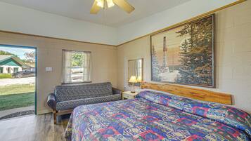 A bedroom with a bed, a sofa, a nightstand, a ceiling fan, and a large window.