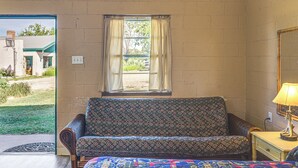 A room with a patterned sofa, a small bedside table with a lamp, a window with curtains, and a view of the outside. - Easy Lake & Hiking Trails Access: Whitney Studio (Whitney)